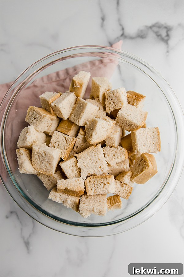 Gluten-free bread cubes soaking in egg mixture in a large bowl, ready for baking.