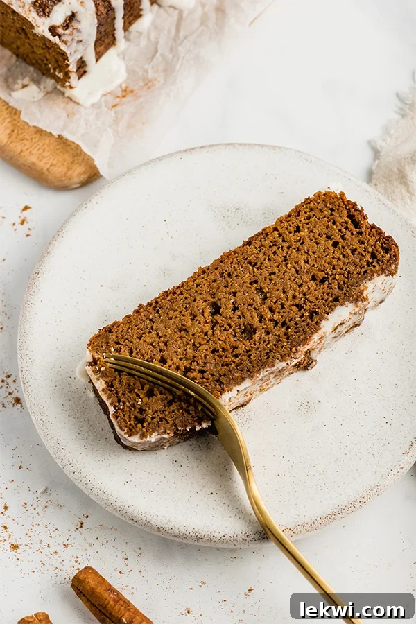 A beautifully sliced piece of paleo sweet potato gingerbread on a white plate, with a fork gently cutting into it, highlighting its soft texture and inviting warmth.