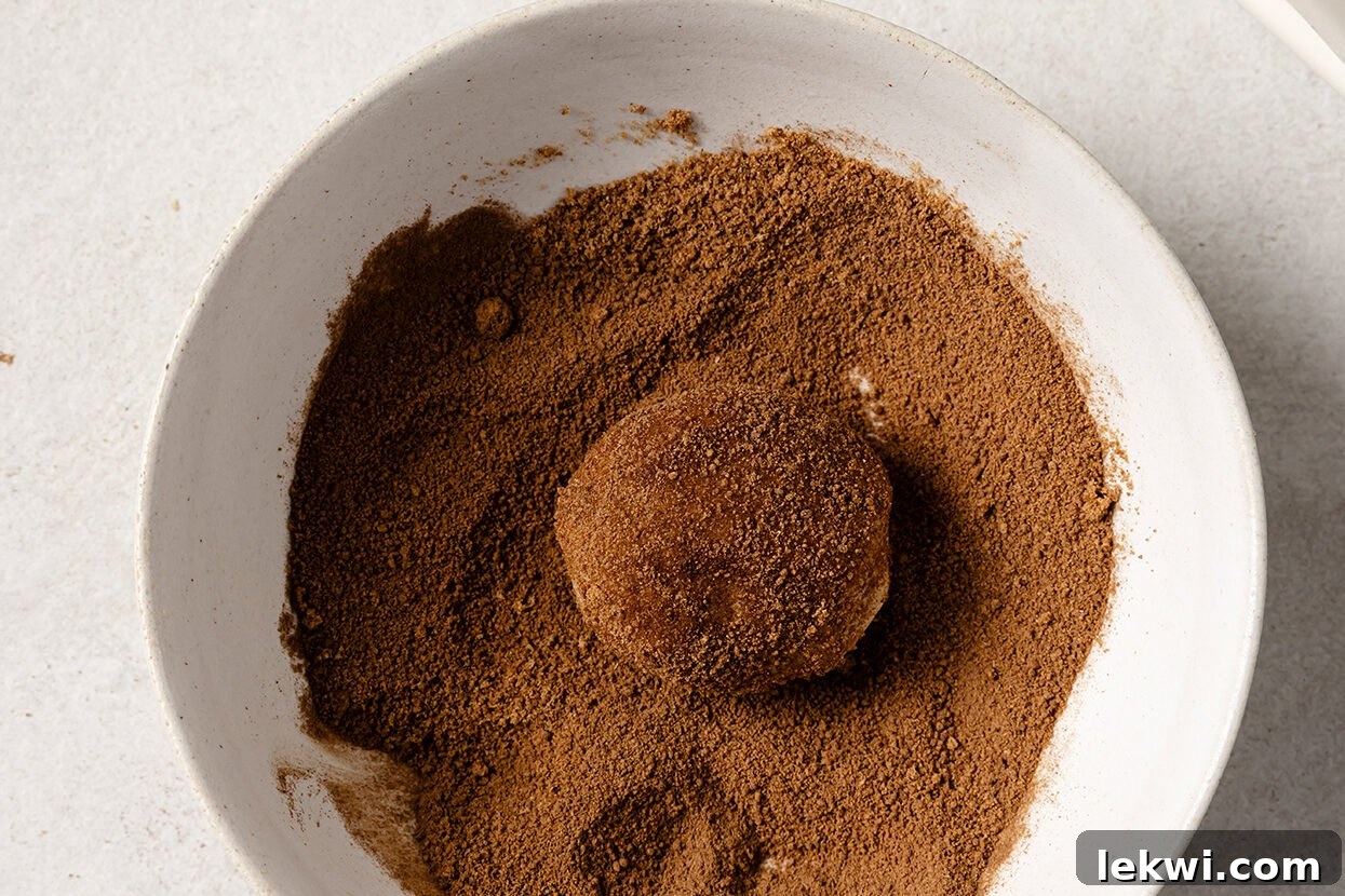 A ball of snickerdoodle cookie dough being rolled generously in a cinnamon-sugar mixture.