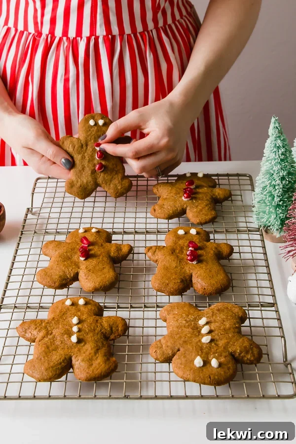 A woman in a festive red and white dress joyfully holds a freshly baked AIP gingerbread cookie, embodying the spirit of holiday baking.