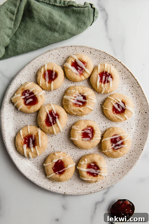 A generous plate of gluten-free thumbprint cookies, each adorned with a bright red jam center and a delicate white drizzle, ready to be enjoyed.