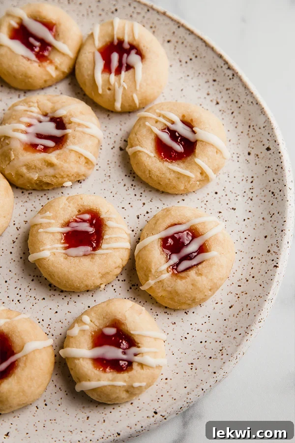 A plate with gluten-free thumbprint cookies with red jam and a white drizzle.