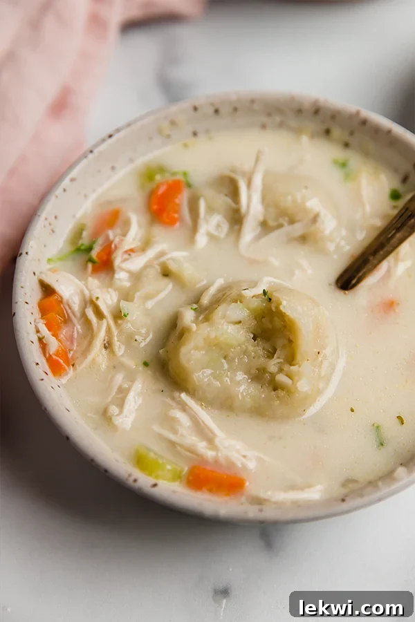 A comforting bowl of gluten-free chicken and cauliflower dumplings soup, garnished with fresh parsley. A close-up shot of a dumpling with a bite taken out reveals its soft texture.