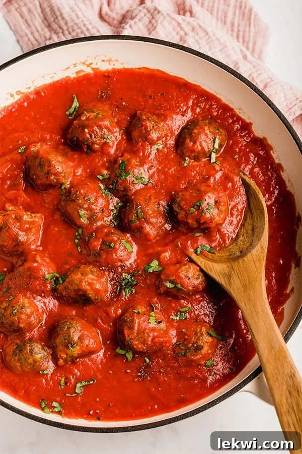 Oven baked meatballs in a pan with a wooden spoon topped with parsley.