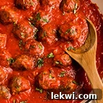 Oven baked meatballs in a pan with a wooden spoon topped with parsley.