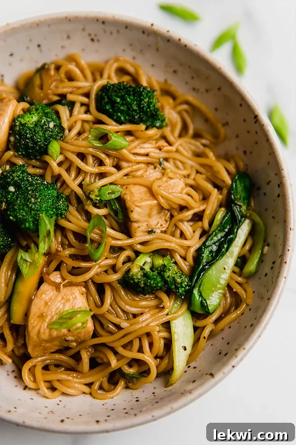 A close-up of a vibrant bowl of chicken and broccoli ramen stir fry, garnished with fresh green onions, ready to be enjoyed.