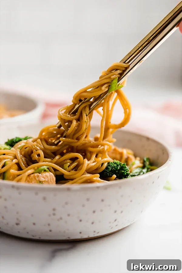 Chicken and ramen stir fry in a bowl with chopsticks, showing the texture and ingredients of the dish.
