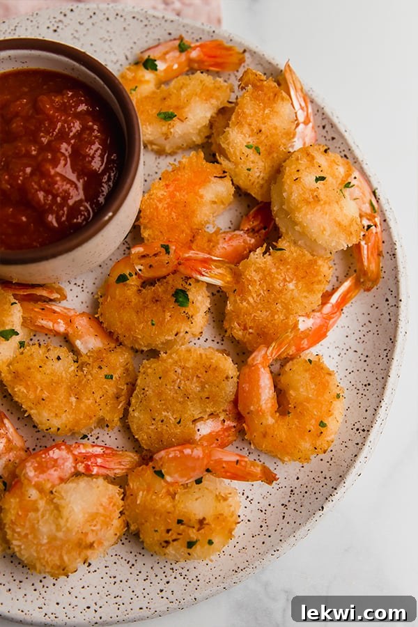 Oven baked coconut shrimp on a plate with a side of sauce, showcasing golden-brown coating.