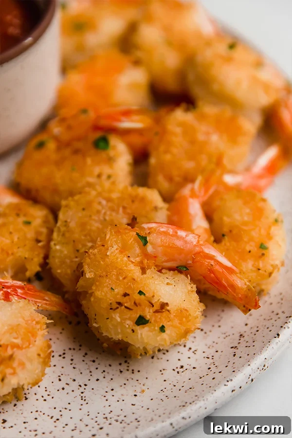 Two plates of oven-baked coconut shrimp, one with dipping sauce, elegantly presented.