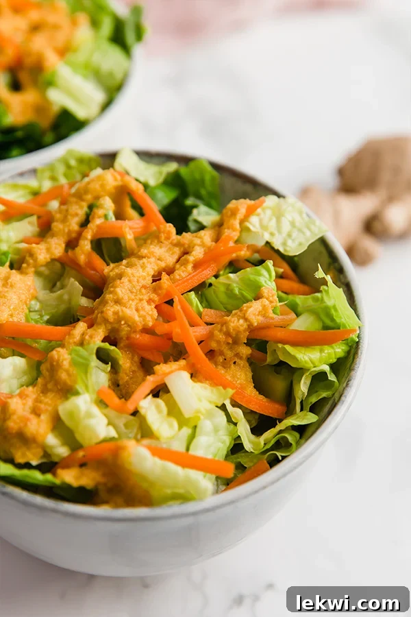 A fresh green salad generously coated with Japanese Restaurant Style Ginger Salad Dressing in a white bowl, ready to be enjoyed.