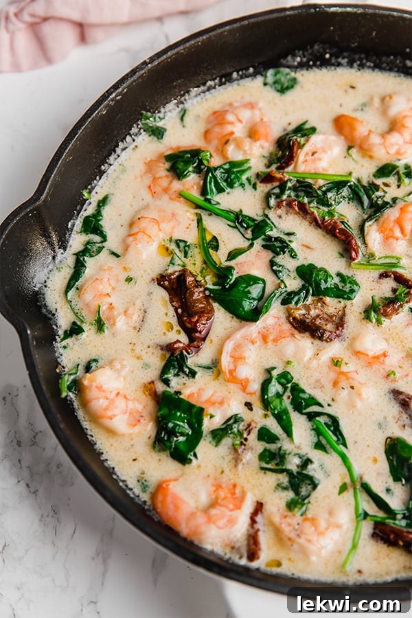 Tuscan Garlic Shrimp sizzling in a cast iron skillet, garnished with fresh herbs, ready to be served.