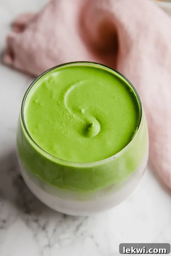 A refreshing Dalgona Matcha drink in a clear glass cup, topped with a beautiful layer of whipped matcha foam, ready to be enjoyed.