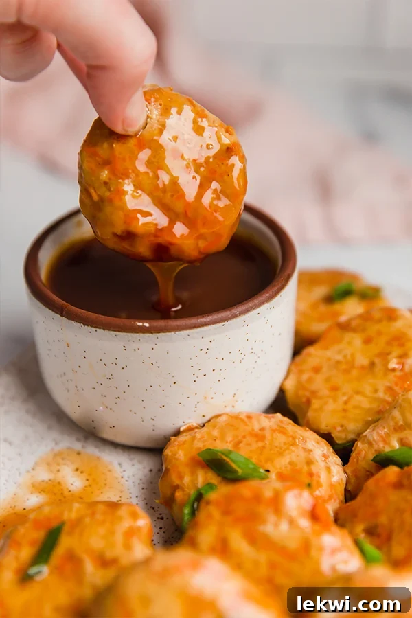 Sweet and sour chicken poppers on a plate, with one piece being dipped into a small bowl of sauce.