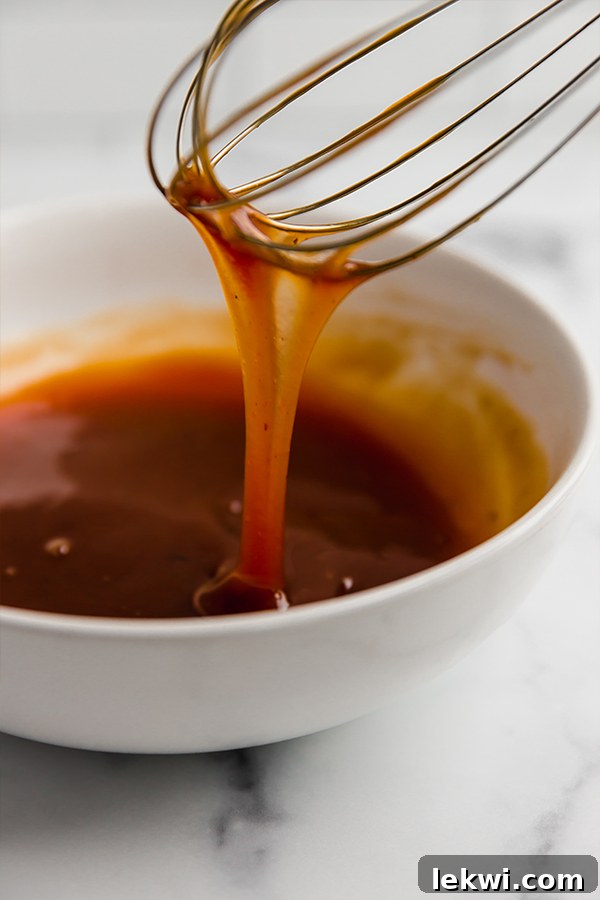 Close-up of sweet and sour sauce with a whisk in a pot.
