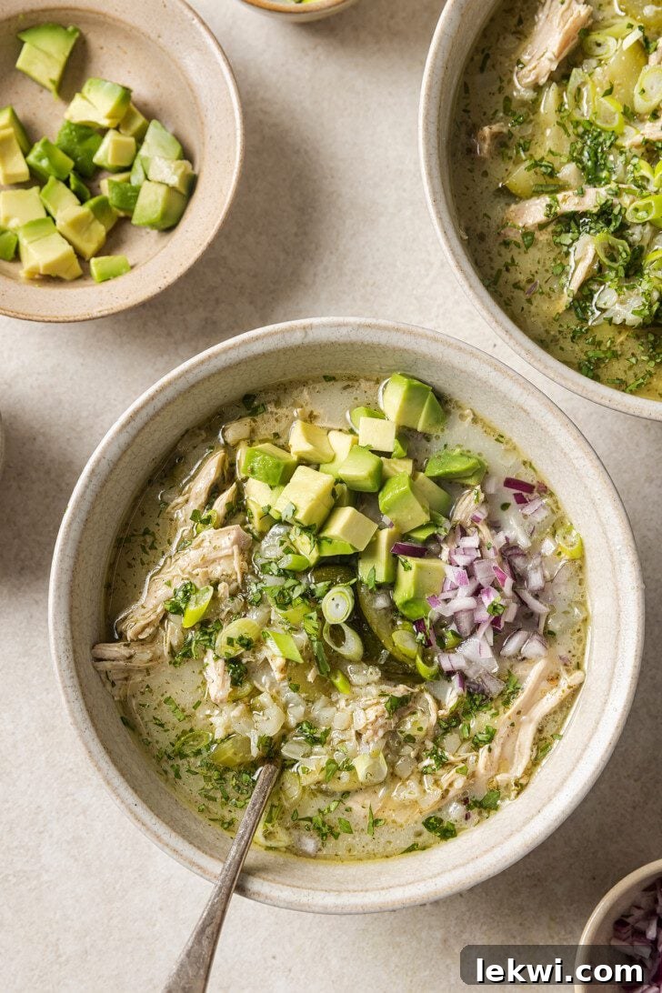 Three bowls of wholesome white chicken chili, generously topped with fresh red onion and creamy avocado, ready for serving.