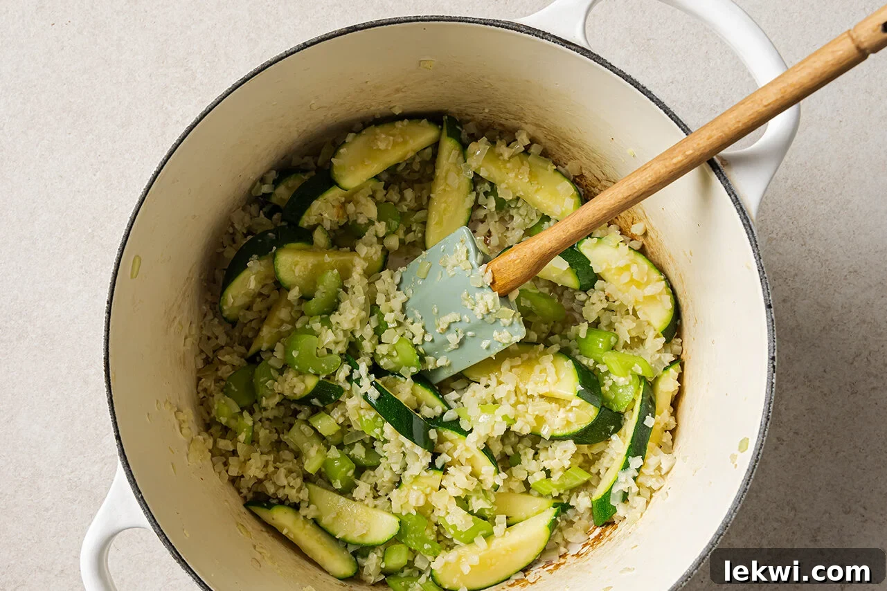 Diced onions, garlic, celery, and zucchini sautéing in a Dutch oven with avocado oil, creating a fragrant base for the chili.