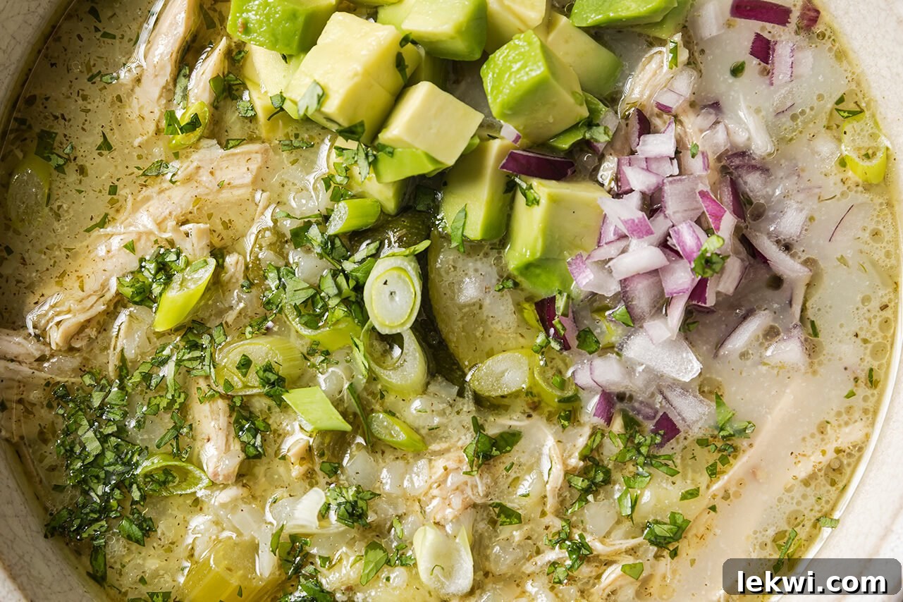 A freshly made bowl of white chicken chili, generously topped with vibrant red onion and creamy avocado slices, ready to be served.