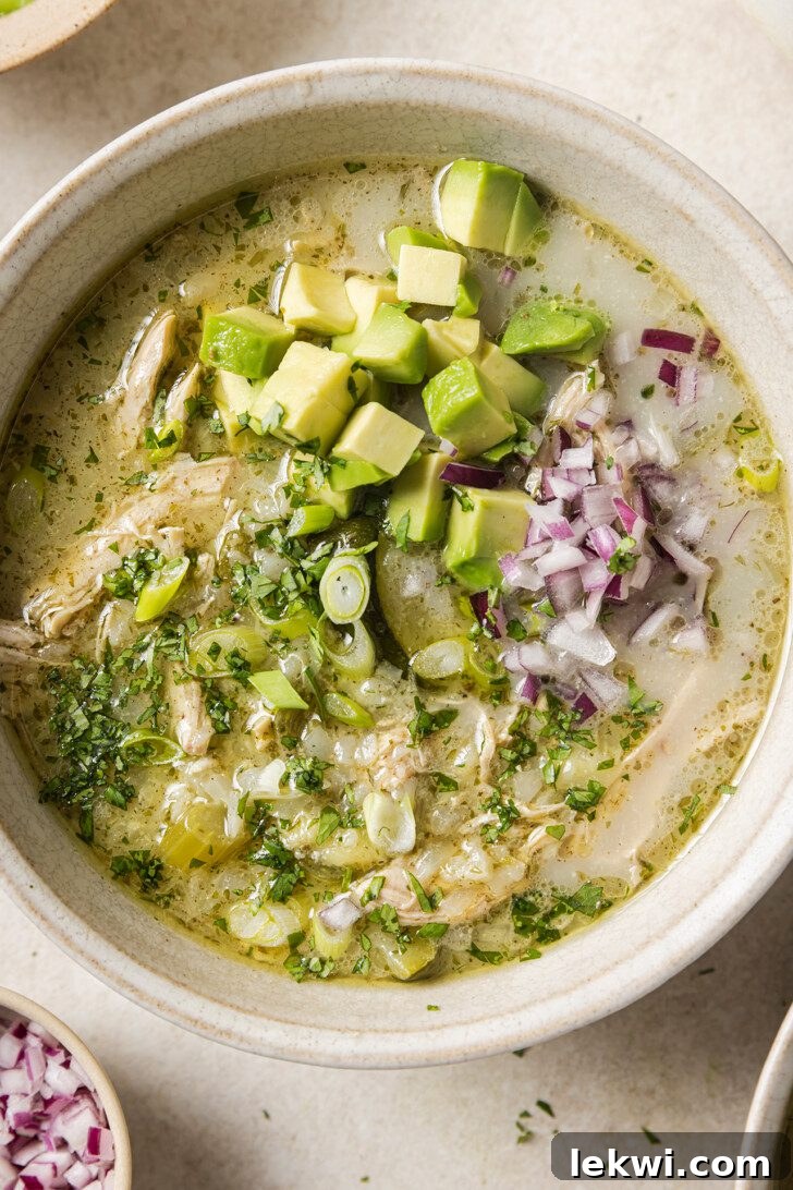 A vibrant bowl of healthy white chicken chili, beautifully garnished with fresh red onion and creamy avocado slices, highlighting its appealing presentation.