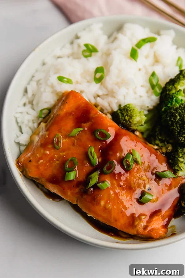 A beautifully presented Teriyaki Salmon Bowl featuring perfectly cooked salmon, fluffy cauliflower rice, and bright green steamed broccoli, elegantly garnished with freshly chopped green onions.