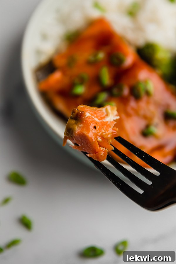 A close-up shot capturing a delicious bite of teriyaki-glazed salmon on a fork, with a blurred yet enticing teriyaki salmon bowl serving as the background.