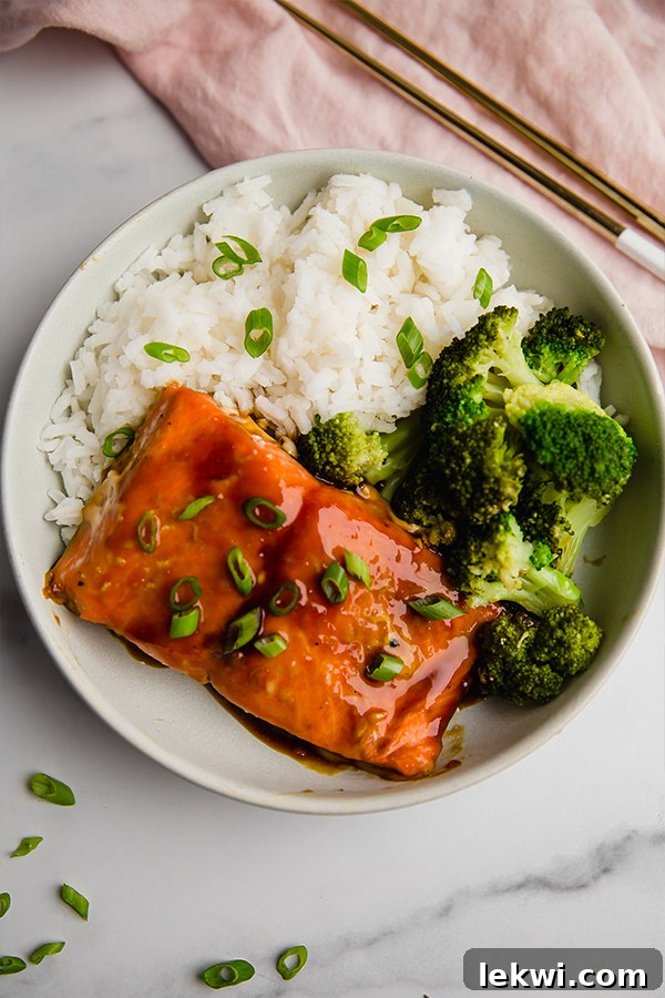A beautifully composed Teriyaki Salmon Bowl, showcasing vibrant broccoli and a fluffy rice base alongside the perfectly cooked salmon, with chopsticks resting gracefully on the side.