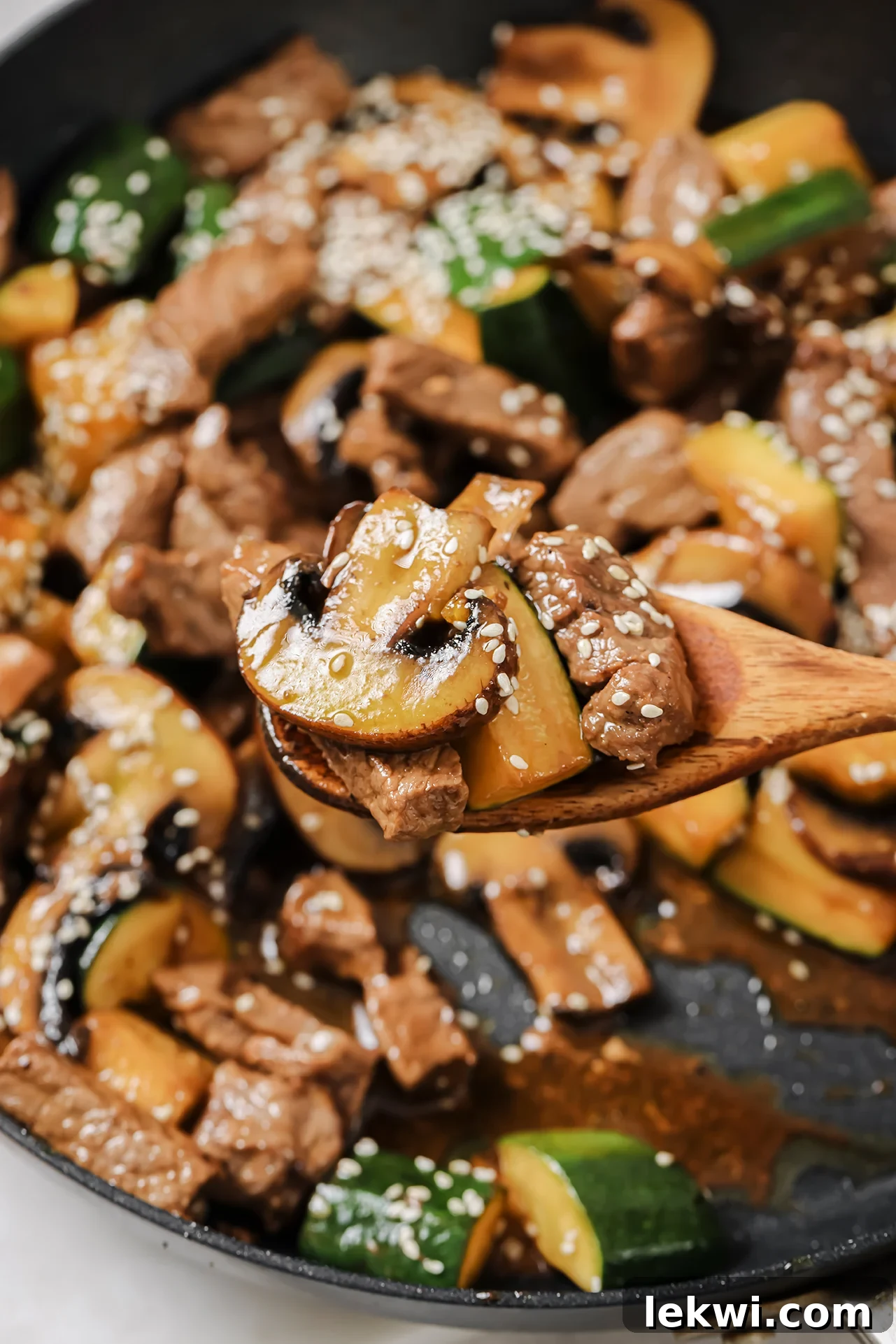 Sizzling hibachi steak and perfectly cooked vegetables being scooped from a pan with a wooden spoon, showcasing a delicious one-pan meal.