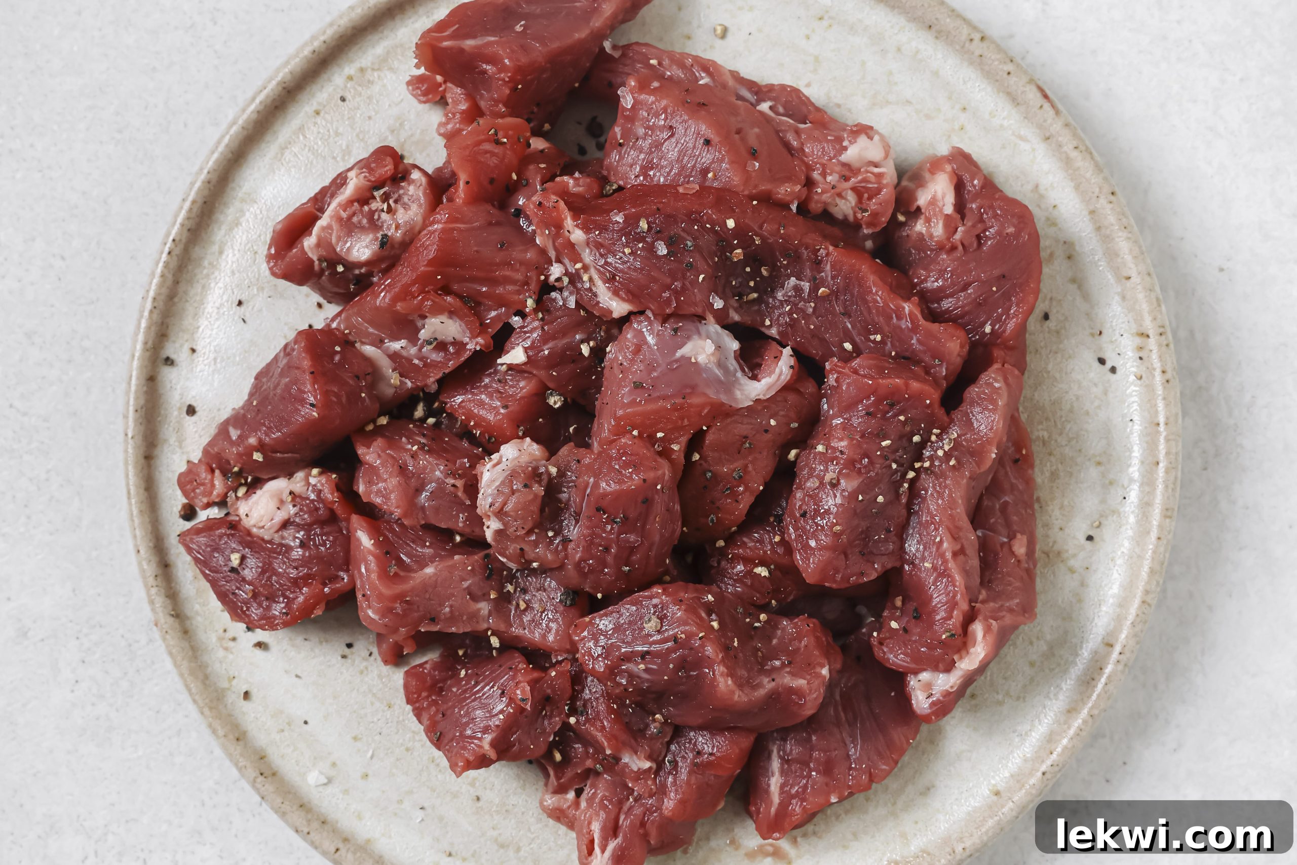 Raw sirloin steak cut into uniform bite-sized pieces, generously seasoned with salt and pepper, ready for cooking.
