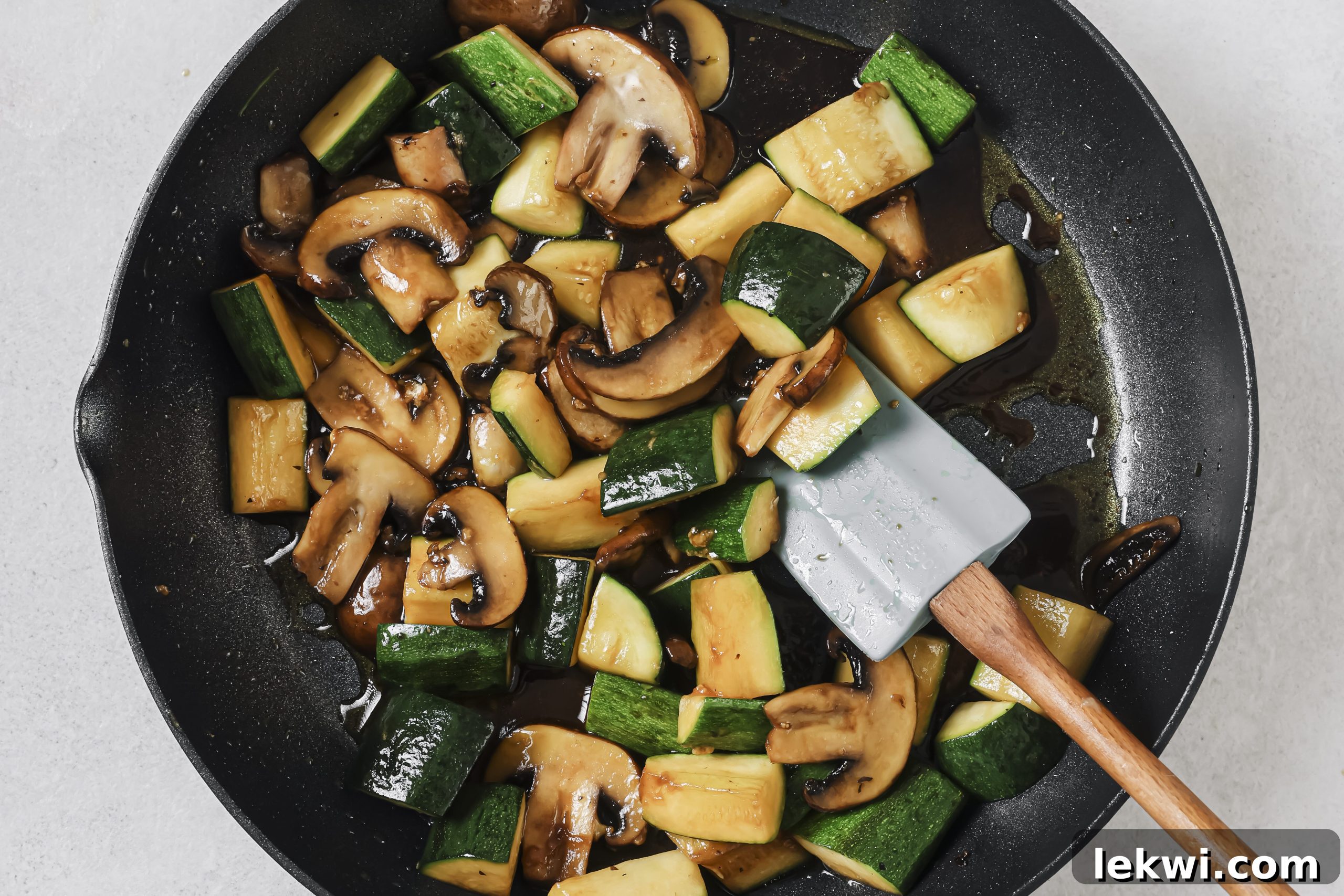 Vibrant zucchini strips and sliced mushrooms sizzling in a hot black pan, gently stir-fried until tender-crisp.