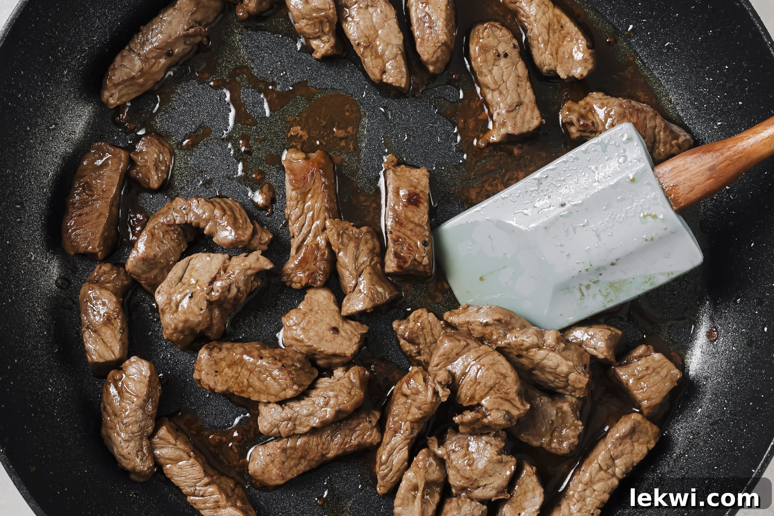 Cubed sirloin steak searing in a black pan, coated in a savory sauce with garlic powder, coconut aminos, and ghee.