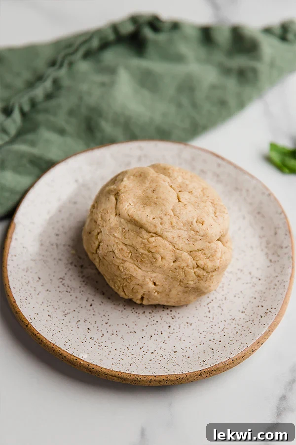 A perfectly formed ball of raw pizza dough resting on a piece of parchment paper on a baking sheet, ready for flattening.