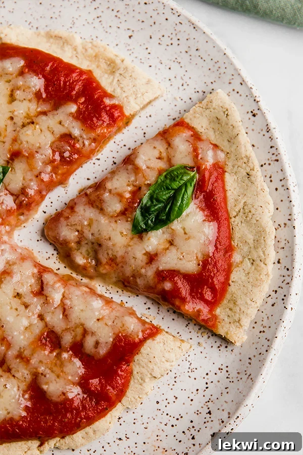 A delicious slice of AIP tigernut flour pizza on a white plate, topped with a piece of fresh basil, indicating a healthy and flavorful meal.