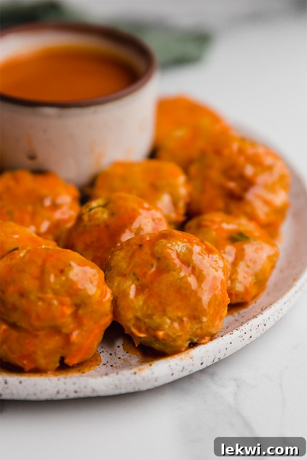 A close-up of buffalo chicken poppers piled high on a plate, with sauce drizzled over them.