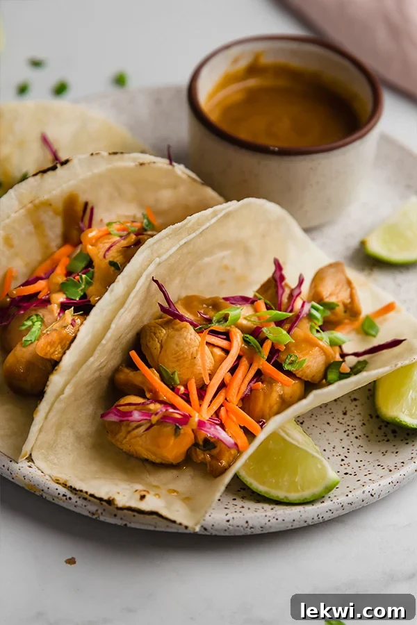 Three beautifully arranged Thai chicken tacos, served on a white plate with a side of almond butter dipping sauce, highlighting the colorful fillings.