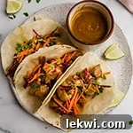 Three Thai chicken tacos on a plate with sauce on the side.