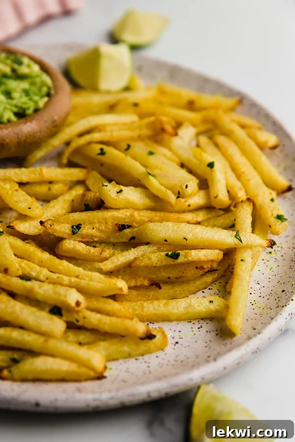 A close-up of jicama fries on a plate, garnished with fresh cilantro and served with a side of creamy guacamole for dipping.