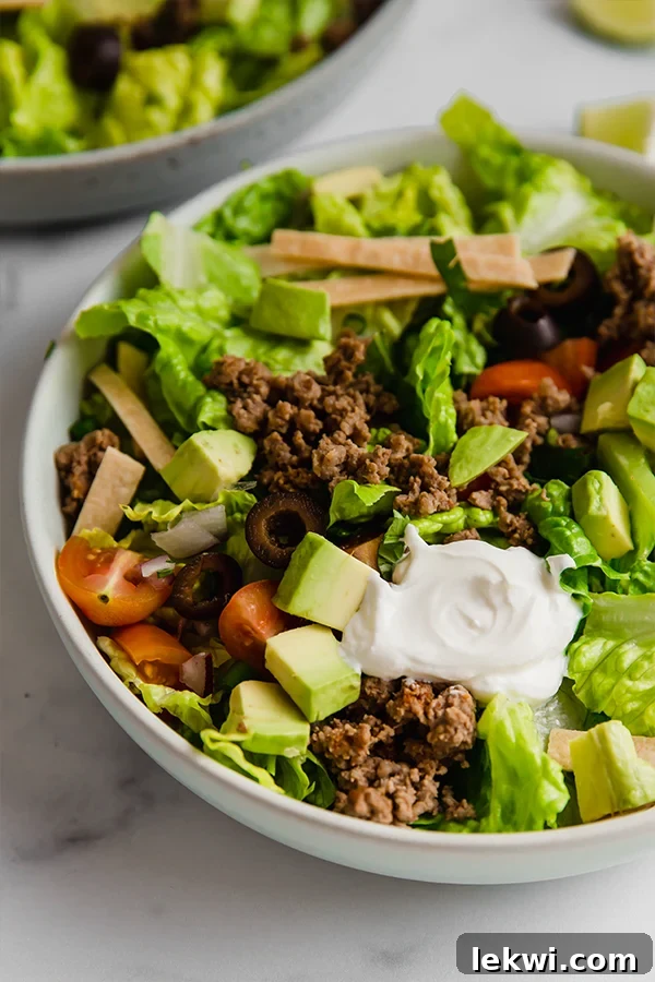A close-up shot of a healthy taco salad served in a rustic bowl, highlighting the fresh ingredients like seasoned ground beef, lettuce, avocado, and olives.