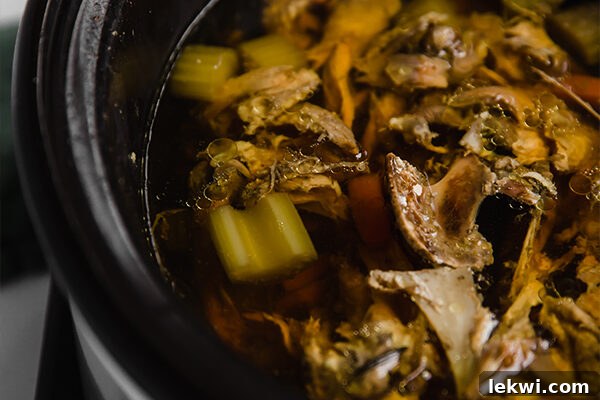 The chicken carcass and vegetables simmering continuously in the golden broth within the slow cooker.