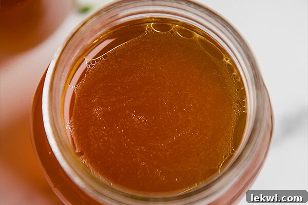 Clear, golden chicken bone broth being carefully poured into a clean glass jar, showcasing its rich color and inviting texture.