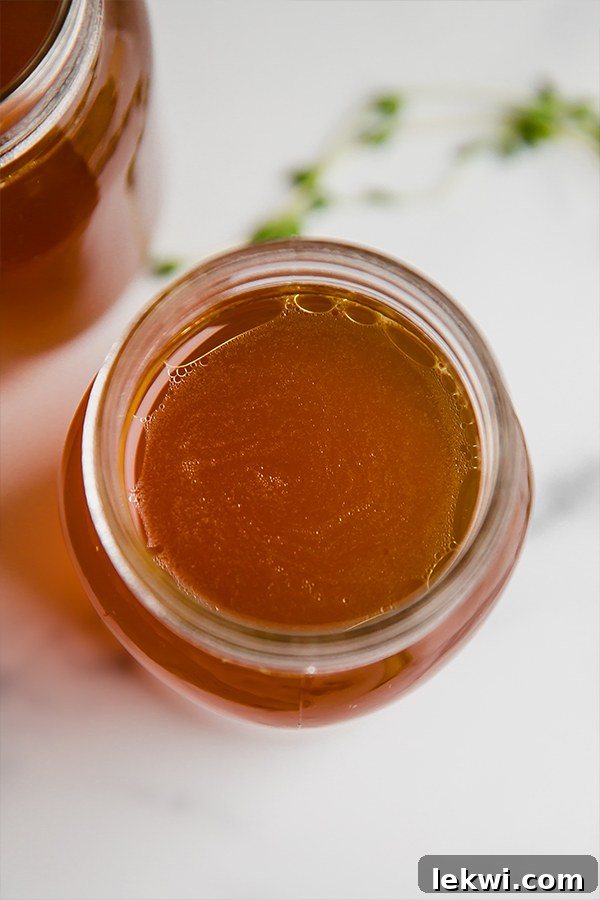 Several glass jars of golden, gelatinous bone broth cooling on a countertop, ready for storage.