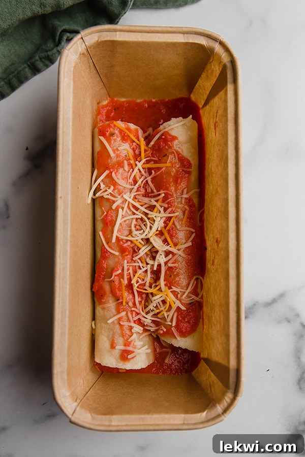 Three individual freezer-friendly chicken enchiladas, each neatly placed in a small loaf pan and covered with aluminum foil, organized in a freezer, ready for future meals.