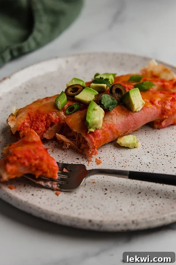 A single, delicious chicken enchilada beautifully presented on a white plate, cut open to reveal the rich, flavorful filling, with a fork beside it, inviting a taste.