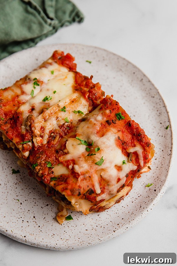 A close-up of two lasagna roll-ups on a white plate, showcasing the layers of pasta, sauce, and cheese, garnished with fresh herbs.