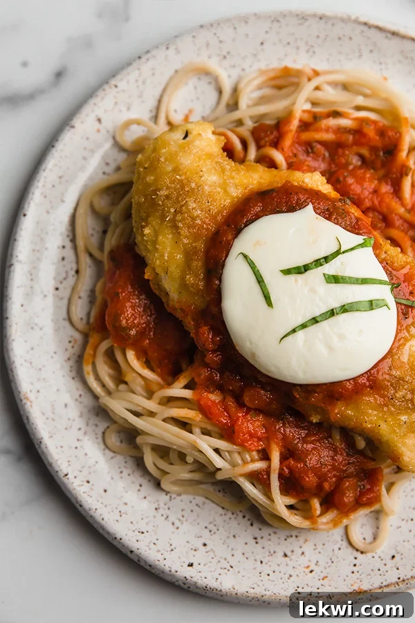 Delicious low-carb chicken parmigiana served over zucchini noodles on a white plate, garnished with fresh basil. The chicken is golden brown with melted cheese and red sauce.
