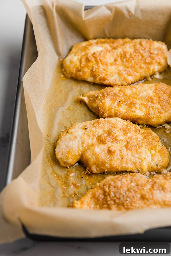 Chicken parmesan baking in a glass casserole dish, with half of the chicken already topped with marinara and melted mozzarella, fresh out of the oven.