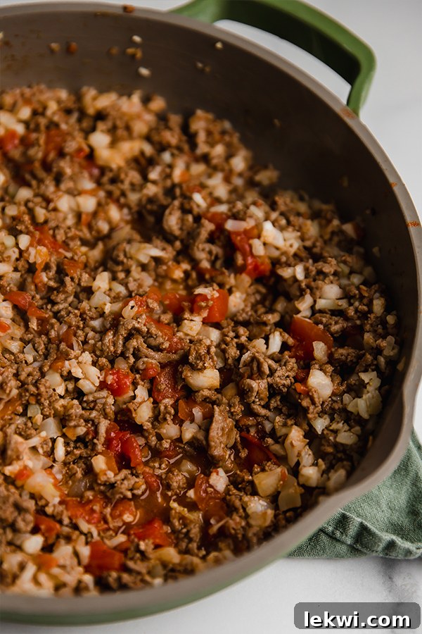 Ground beef and cauliflower rice cooking in a large pan with diced onions and spices.