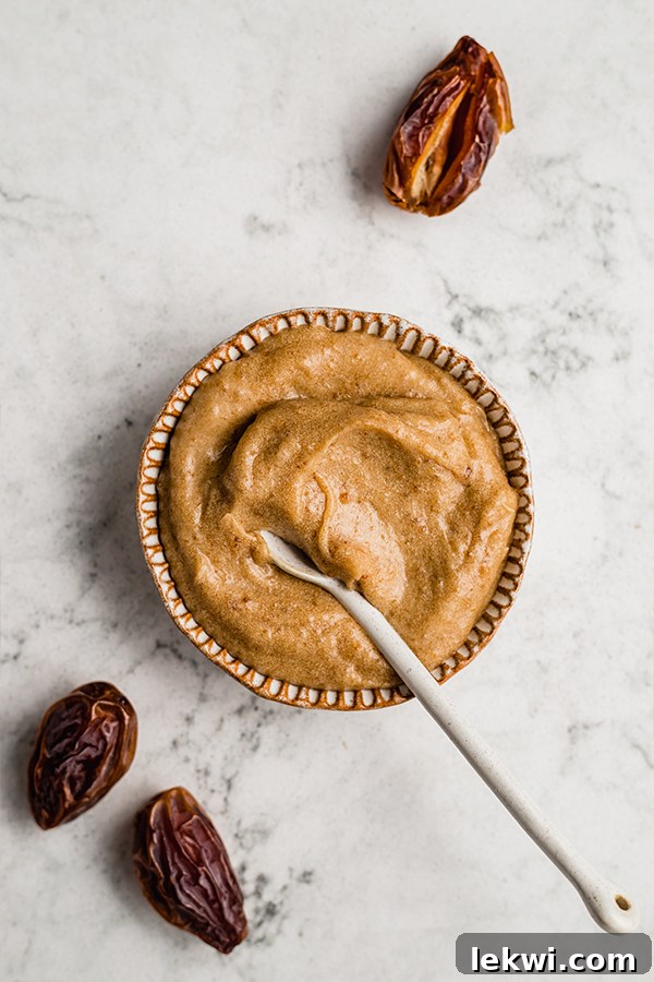 A spoon resting in a bowl filled with creamy, light brown date and coconut milk caramel, ready for assembly.