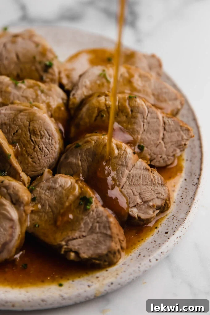 Sliced Instant Pot Pork Tenderloin with gravy and fresh herbs, served on a plate with toothpicks