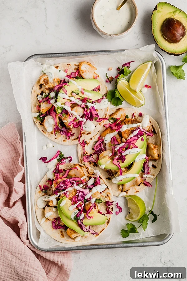 A vibrant platter of three fish tacos, garnished with fresh avocado slices, bright lime wedges, and a sprinkle of cilantro, accompanied by the creamy sauce.