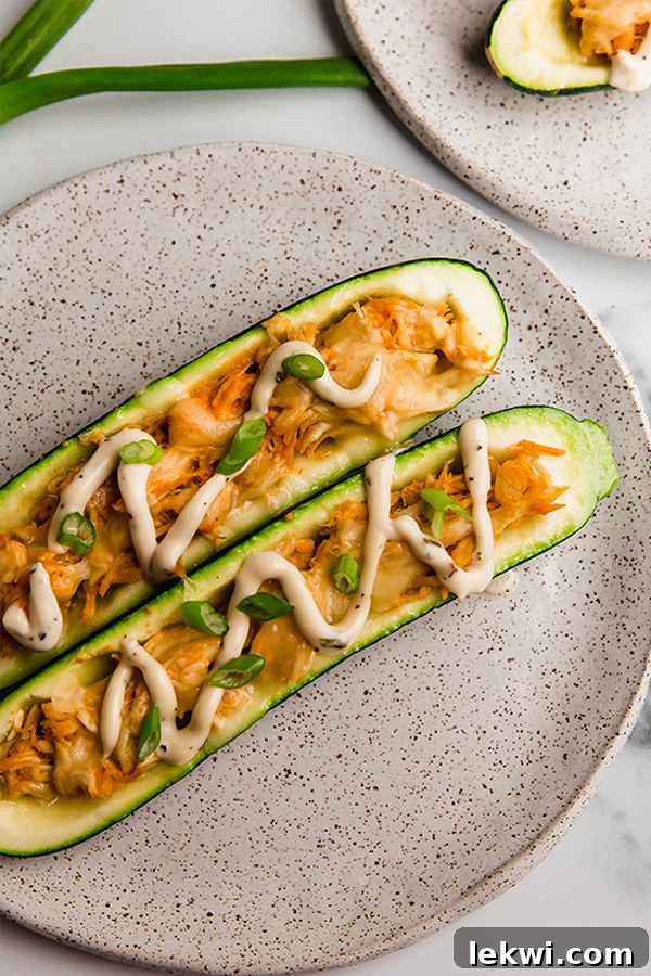 Close up image of the finished Buffalo Chicken Stuffed Zucchini Boat on a plate, garnished with ranch and green onions.