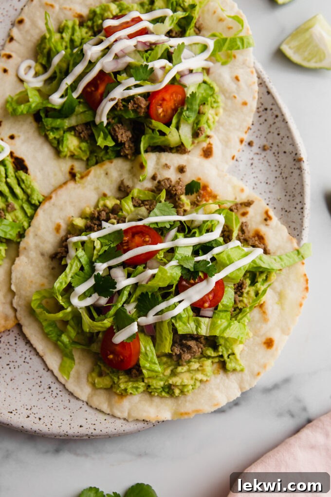 Three perfectly assembled paleo ground beef tostadas on a rustic plate, garnished with fresh cilantro and lime.